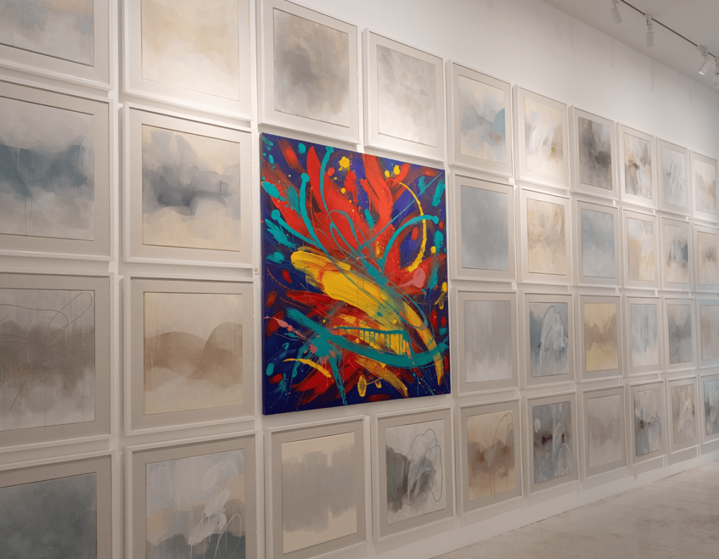 A wall of paintings that all look the same. One vibrant abstract painting that stands out